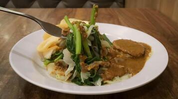 Indonesisch voedsel borst, traditioneel Javaans schotel bestaat van mengen vers groenten en pinda saus dressing, met extra kerupuk of crackers, Aan de bord. foto