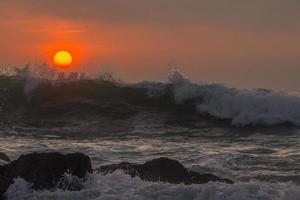 golven spatten in de rotsen bij zonsondergang foto