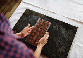 detailopname van vrouw handen Holding chocola mallen vol van vloeistof verwarmde chocola massa. voorbereidingen treffen chocolaatjes voor vieren wereld chocola dag foto