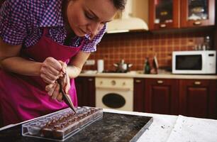 chef gebakje knijpen zoet romig vloeistof van banketbakkerij zak in snoep mallen voor maken luxe pralines en truffels Bij huis foto