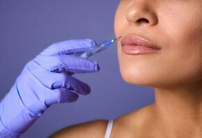 injectie cosmetologie, esthetisch chirurgie, lippen vergroting en correctie concept. detailopname van vrouw gezicht en hand- in chirurgisch handschoen Holding injectiespuit in de buurt haar lippen, klaar naar te ontvangen schoonheid behandeling foto