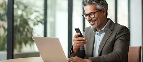 volwassen zakenman gebruik makend van mobiel app en laptop in kantoor glimlachen foto