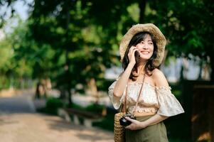 portret van Aziatisch jong vrouw reiziger met het weven hoed, mand, mobiel telefoon en camera Aan groen openbaar park achtergrond. reis reis levensstijl, wereld reizen ontdekkingsreiziger of Azië zomer toerisme concept. foto