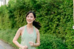 fit Aziatisch jong vrouw jogging in park glimlachen gelukkig rennen en genieten van een gezond buitenshuis levensstijl. vrouw jogger. geschiktheid loper meisje in openbaar park. gezond levensstijl en welzijn wezen concept foto