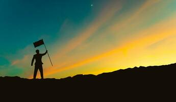 silhouet van zakenman met vlag Aan berg top over- zonsondergang lucht achtergrond, bedrijf, succes, leiderschap en prestatie concept foto