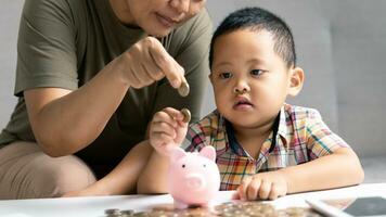 gelukkig Aziatisch kind en mam besparing geld samen, zetten contant geld in varkentje bank. moeder spelen met kind Aan verwarming verdieping Bij huis, onderwijs weinig zoon naar investeren geld, planning toekomst. foto