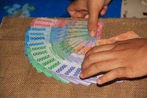 bandoeng, Indonesië - juli 2023 dichtbij omhoog visie van volwassen handen regelen van roepia bankbiljetten voor bruiloft bruidsschat. foto