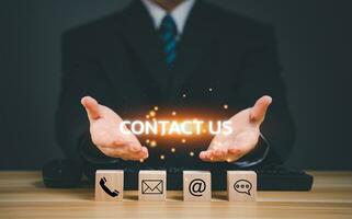 contact ons, onderhoud steun, bedrijf communicatie, klant ondersteuning concept. bedrijf Mens hand- Holding tekst contact ons naar klant ondersteuning online internet met hout blok telefoon, e-mail, massage icoon. foto