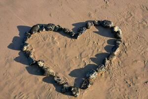 hart gemaakt van rotsen Aan zand strand foto