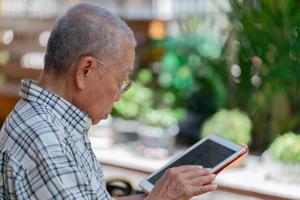 senior aziatische man die tablet gebruikt om tijdens vrije tijd thuis sociale media te spelen