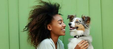 jong vrouw van Afrikaanse afdaling bewondert komisch afdrukken van hond speels emuleert zoenen gebaar tegen licht groen backdrop buitenshuis portret van aantrekkelijk foto