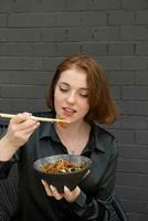 mooi jong vrouw smaakt udon noedels met vlees en gebakken groenten foto