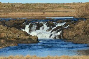 Ondiep waterval over- rotsen langs weg in IJsland foto