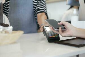 vrouw klant Holding telefoon in de buurt nfc terminal maken contactloos mobiel betaling. foto