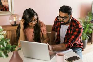 millennial Indisch man en vrouw aan het doen huiselijk papierwerk, accounting baan en herzien papier rekeningen, bonnen Bij laptop computer, gebruik makend van online rekenmachine - economisch crisis concept foto