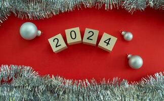 nieuw jaar kaart 2024. houten kubussen met getallen 2024, klatergoud en nieuw jaar ballen Aan een rood achtergrond. foto
