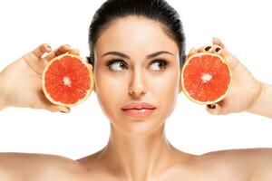 gezond voedsel concept. mooi jong vrouw Holding stuk van grapefruit dichtbij naar gezicht, geïsoleerd over- wit achtergrond foto