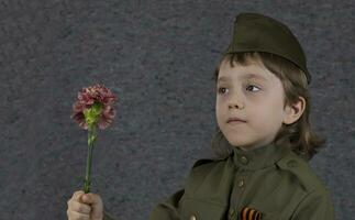 een jong jongen in een leger uniform Holding een bloem foto