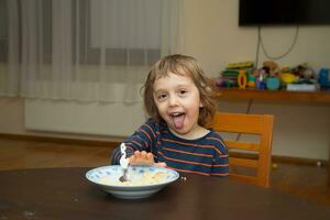 een jong jongen zittend Bij een tafel met een kom van ontbijtgranen foto