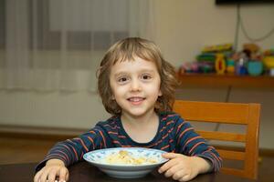 een jong jongen zittend Bij een tafel met een kom van voedsel foto
