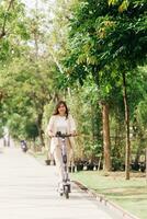 Aziatisch vrouw rijden elektrisch scooter in de park, levensstijl concept foto