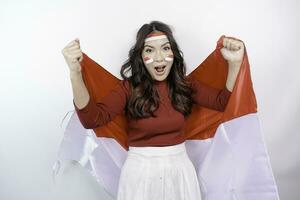 een jong Aziatisch vrouw met een gelukkig geslaagd uitdrukking vervelend rood top en hoofdband terwijl Holding Indonesië's vlag, geïsoleerd door wit achtergrond. Indonesië's onafhankelijkheid dag concept. foto