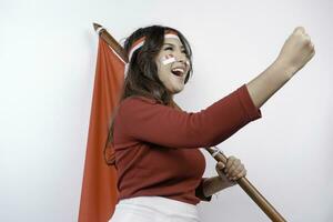 een jong Aziatisch vrouw met een gelukkig geslaagd uitdrukking vervelend rood top en hoofdband terwijl Holding Indonesië's vlag, geïsoleerd door wit achtergrond. Indonesië's onafhankelijkheid dag concept. foto