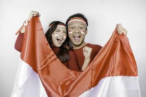 een jong Aziatisch paar met een gelukkig geslaagd uitdrukking vervelend rood top en hoofdband terwijl Holding Indonesië's vlag, geïsoleerd door wit achtergrond. Indonesië's onafhankelijkheid dag concept. foto