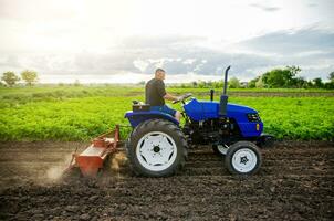 een boer Aan een trekker cultiveert een veld. boerderij werk. frezen bodem, verzachtend de bodem voordat aanplant nieuw gewassen. landbouw. ploegen. losmaken oppervlak, land- teelt. mechanisatie in landbouw. foto