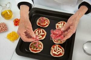 toevoegen toppings naar de mini pizza's. toevoegen salami. heerlijk eigengemaakt mini pizza's voorbereiding. foto