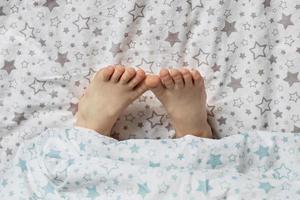 close-up van de voeten van een peutermeisje op het bed onder de deken foto