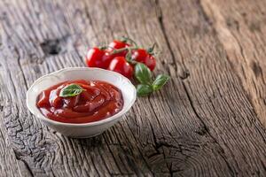 ketchup of tomaat saus in wit kom en kers tomaten Aan houten tafel. foto