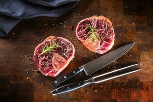 twee rauw stukken rundvlees schacht Aan houten slager bord met vork en mes. foto