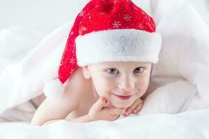 schattig baby jongen met de kerstman hoed Aan bed onder wit dekbed foto