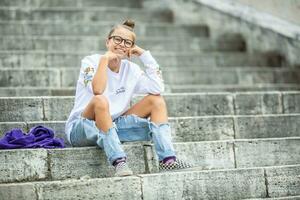 jong tiener- meisje zittend Aan de stappen in de park en glimlachen foto
