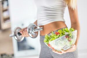 vrouw Holding kom van vers groente salade en halter. foto