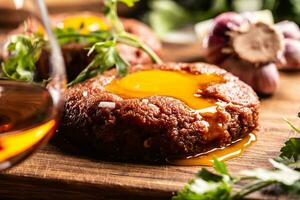 extreem heerlijk rundvlees steak tartaar met lief ei dooier geserveerd Aan houten bureau met kruiden en knoflook in de achtergrond. rum net zo een drank foto