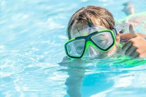 kind zwemmen in een zwembad met stofbril Aan tonen duimen omhoog gebaar foto