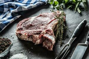 rib oog steak met bot Aan slager bord met kruiden zout peper vork en mes foto