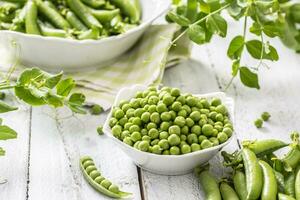 groen rauw erwten en peulen in pocelain boog geïsoleerd Aan houten tafel foto