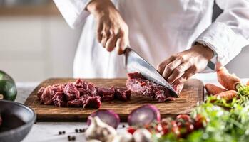 chef snijdend rood vlees naar klein brokken naar bereiden stoofpot of goulash foto