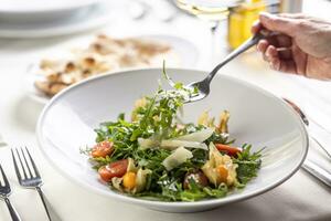 hand- nemen een vork met ruccola uit van een raket salade in een bord foto