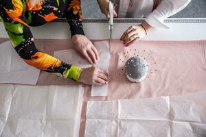 top visie van de werk van kleermakers in de werkplaats meten, snijdend en naaien kleren van de kleding stof Aan de tafel gebaseerd Aan papier sjabloon foto