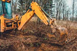 de graafmachine graaft grond in het bos en ontwortelt de wortels van de bomen. foto