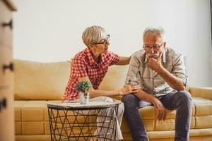 senior paar zittend in leven kamer. Mens is verdrietig en bezorgd en vrouw is troostend hem. foto