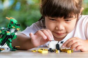 dichtbij omhoog Aziatisch meisje 5-6 jaar oud kind spelen met Lego bakstenen of speelgoed- Bij huis, Aziatisch meisjes kom tot rust met spelen steen blokken Aan houten tafel en genieten spelen speelgoed. foto