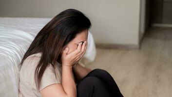 verdrietig depressief Azië vrouw lijden Aan de wit bed, ze is zittend in bed en aanraken haar voorhoofd, slaap wanorde en spanning concept foto