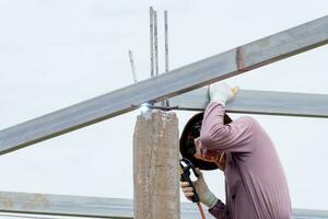 bouw arbeider mannen lassen dak staal balken, Mens werken met een lassen machine en metaal, huis Bouwers zijn lassen staal structuren voor huis bouw, zonder vervelend veiligheid uitrusting foto