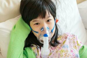 ziek weinig Aziatisch meisje inademing met vernevelaar voor ademhalings behandeling foto