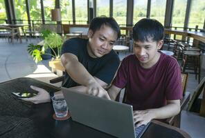 jong Aziatisch Mens werken van een afstand Aan internet online over- laptop Aan vakantie terwijl nemen een breken met zijn vriend in cafe Aan berg, bestemming in thailand.concept van reizen vrij, digitaal nomade foto